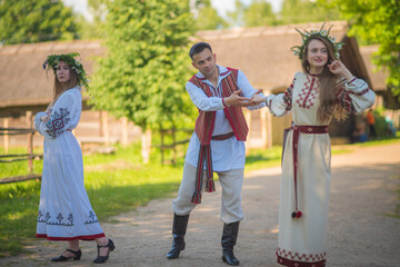 Obraz premium Slavic youth dancing and flirting in traditional embroidered clothes inside historical village with copy space
