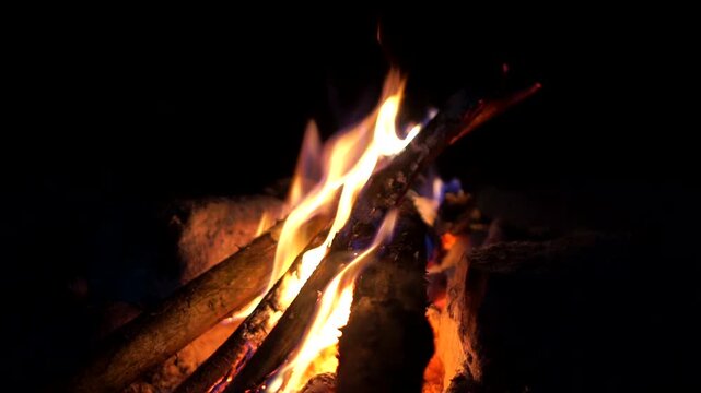 Close-up shot of bright orange flames burning traditional firewood inside a simple outdoor stone hearth.	