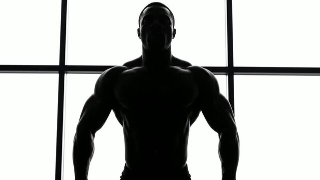 Powerful Bodybuilder Silhouette Posing Against Bright Window With Strong Muscular Definition In Dynamic Display Of Strength And Determination