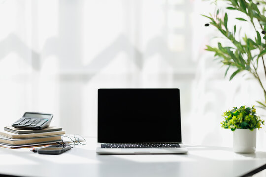 Laptop Computer, notebook, and eyeglasses sitting on a desk in a large open plan office space after working hours