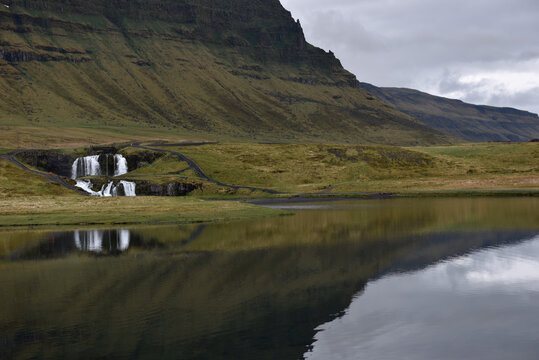 Small waterfall and green hills reflecting in a calm lake, Iceland