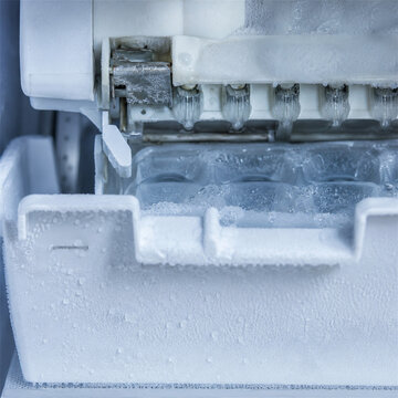 Close up of frosty ice maker tray inside freezer with frozen water buildup showing household appliance maintenance cold texture refrigeration mechanism and kitchen technology detail