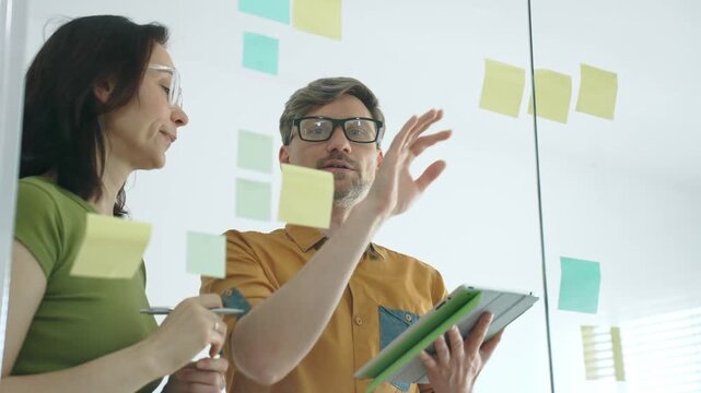 Business team clapping and celebrating after a productive brainstorming session, collaborating around a glass board with sticky notes, charts and strategic planning in a modern office