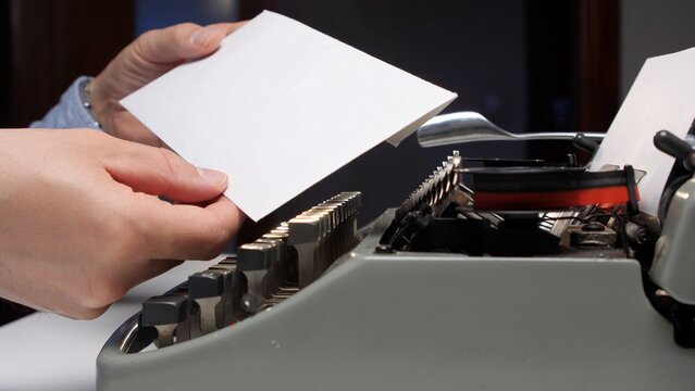 Hand inserting a blank sheet of paper into the platen of an antique manual typewriter, preparing to type a document or letter, highlighting nostalgic writing and communication