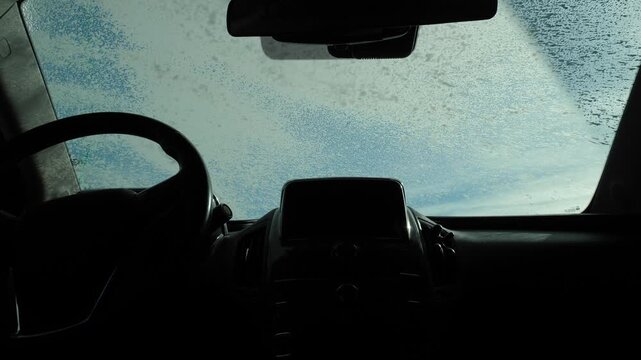 View from inside the car, a man applying foam to the windshield. Car wash outside. Cleaning the car