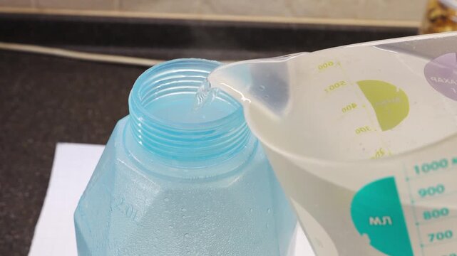 Boiling water is poured from a measuring pitcher into a blue container. It mixes with oxygen bleach to create a powerful solution for cleaning soft furniture and mattresses.