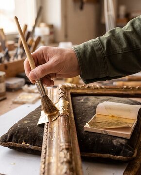 Hand applying gold leaf to ornate antique picture frame macro gilding heritage restoration