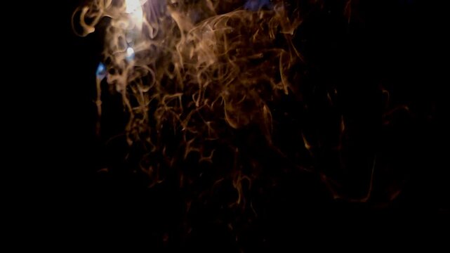 Abstract close-up footage of blue flames and swirling smoke rising from burning plastic against a deep black background. The flowing smoke creates dramatic organic patterns