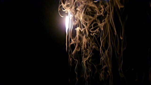 Abstract close-up footage of blue flames and swirling smoke rising from burning plastic against a deep black background. The flowing smoke creates dramatic organic patterns