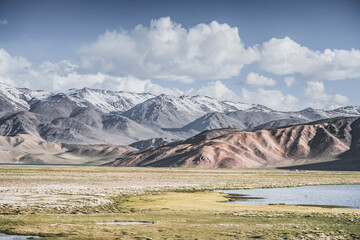 A mountain landscape featuring rocky peaks and snow-capped glaciers, with a valley containing fields, pastures of fresh green grass, and clear-water rivers—suitable for a background image © Denis