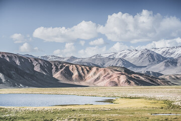 A mountain landscape featuring rocky peaks and snow-capped glaciers, with a valley containing fields, pastures of fresh green grass, and clear-water rivers—suitable for a background image © Denis