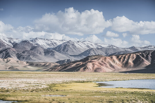 A mountain landscape featuring rocky peaks and snow-capped glaciers, with a valley containing fields, pastures of fresh green grass, and clear-water rivers&mdash;suitable for a background image