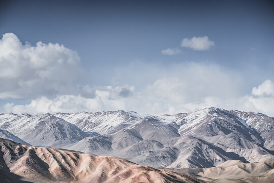 Rocky mountain range with snow and glaciers against a cloudy sky, in the Tien Shan Mountains on Pamirs, stone mountain with red texture, minimalist landscape for background