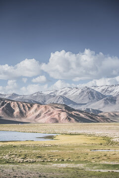 A mountain landscape featuring rocky peaks and snow-capped glaciers, with a valley containing fields, pastures of fresh green grass, and clear-water rivers&mdash;suitable for a background image
