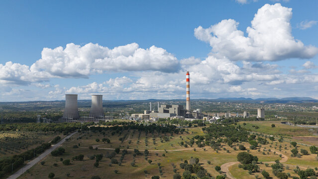 Portugal - 23 June 2026: Aerial view of a natural gas-powered combined cycle plant with cooling towers and a tall chimney stack, set in a rural landscape with olive trees under a blue sky.