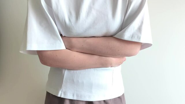 Woman presses both hands against her stomach feeling sudden cramping pain. She bends slightly while holding her abdomen in discomfort. Concept of digestive trouble, bloating and