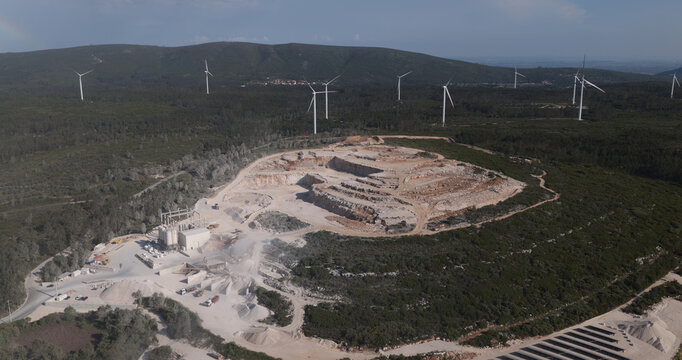 Portugal - 23 June 2026: Aerial view of a quarry mine in the mountains, featuring industrial excavation sites, heavy machinery, and surrounding wind turbines on the hills.