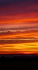 Fototapeta premium A radiant display of vibrant orange, yellow, and deep red hues paints the summer evening sky above the distant, hazy horizon line, natural, vibrant, sky