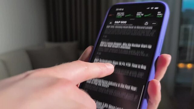 Hand holds smartphone with stock market chart in close up. The screen scrolls through SP 500 data and finance news. Mobile trading and investment analysis concept..