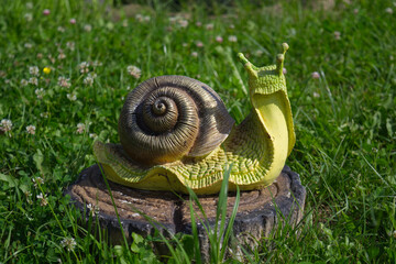 Garden snail figurine resting on a tree stump in green grass. Decorative object perfect for garden, nature, and whimsical themes. © peachbox