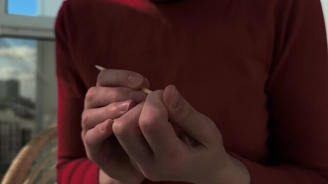 Using wood bamboo cuticle stick for finger nail care in closeup. The manicure routine by self. Personal hygiene and beauty maintenance at home..