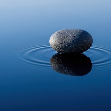 A perfectly smooth stone rests on a calm water surface, creating a flawless reflection showing identity and similarity or the sense of self, resemblance, view, metaphor