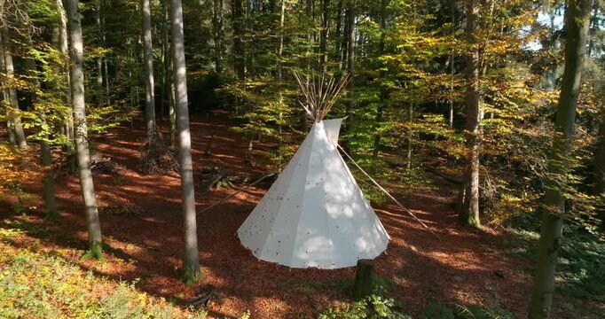 Wei&szlig;es Tipi-Zelt in einem herbstlichen Wald, umgeben von B&auml;umen, Laub und warmer Naturstimmung, als ruhige Outdoor-Szene f&uuml;r Camping, R&uuml;ckzug und Erholung