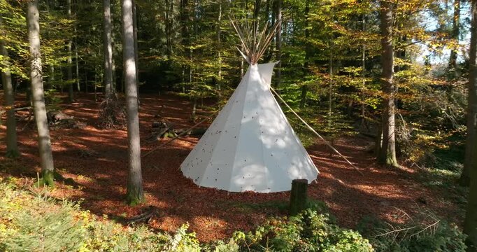 Wei&szlig;es Tipi-Zelt in einem herbstlichen Wald, umgeben von B&auml;umen, Laub und warmer Naturstimmung, als ruhige Outdoor-Szene f&uuml;r Camping, R&uuml;ckzug und Erholung