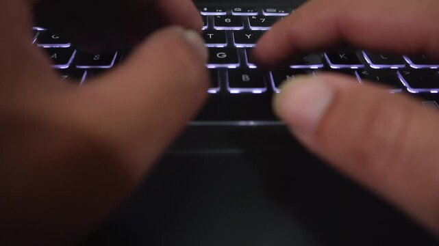 Hands typing rapidly on a backlit keyboard in dim night light.
