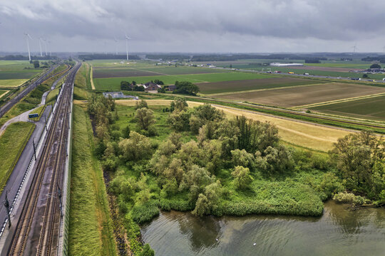 Moerdijk, Netherlands - 27 May 2025: Aerial view of the Moerdijk railway line with Vattenfall wind turbines, green fields, and water under a cloudy sky.
