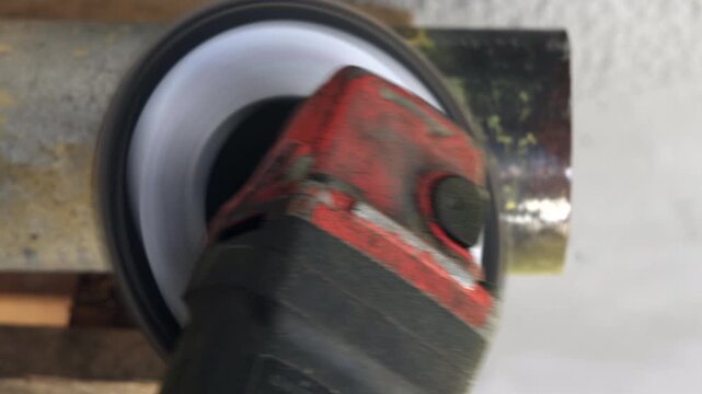 Close up of an angle grinder stripping old paint from a metal pipe surface