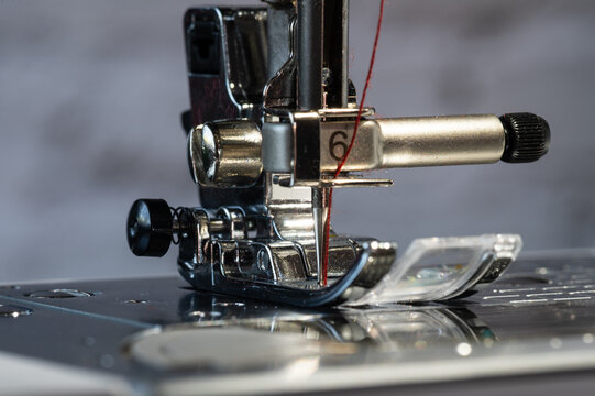 Sewing machine foot with needle at the bottom and red sewing thread in close-up