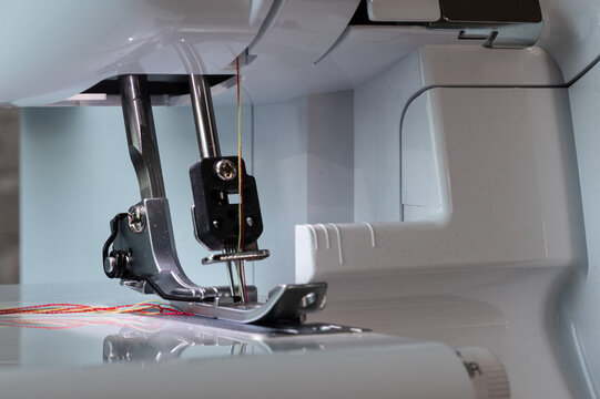 Overlock sewing machine with lowered foot, needles at the bottom, and carrier with close-up view from diagonally left