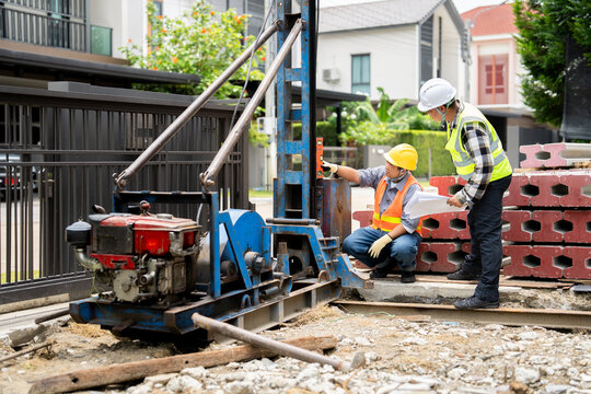 Engineers inspecting a micro pile driving machine.Team of builders inspecting a micro pile driver machine. Engineers with blueprints work on a residential home foundation and structure.