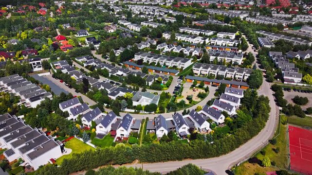 Modern residential neighborhood newly built semi detached houses family homes in suburban area, featuring green gardens, roads, parked cars and a red sports field, perfect for real estate market