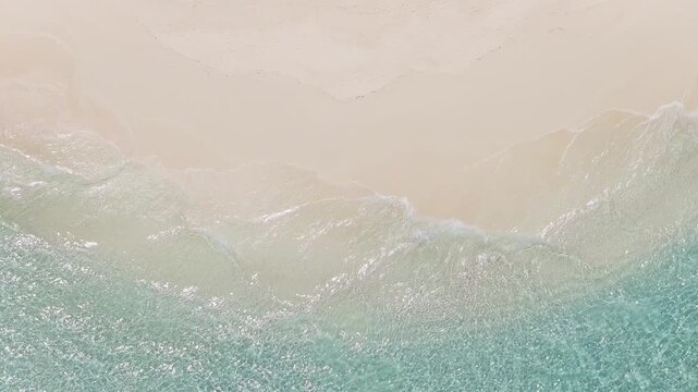 Aerial view of a Maldives atoll shows a powder white beach, shallow glassy water, gentle lace like breakers, sun reflections, and faint footprints from above.