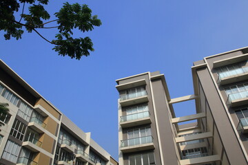 Obraz premium Low angle of modern apartment building under blue sky surrounded by green trees.