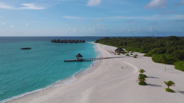 Aerial Maldives atoll shows palm sand crescent, wooden jetty, thatched gazebo, overwater villas, moored dhoni, tiny island on horizon, gentle waves, bright daylight.
