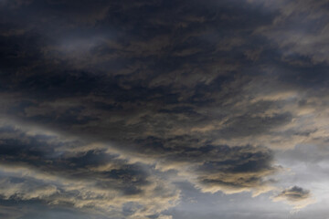 Fototapeta premium Dark turbulent cloudscape with golden-tinged wave-like formations swirling across a brooding sky