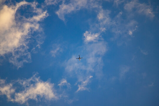 Twin-engine plane seen from ground level against scattered white clouds and deep blue sky