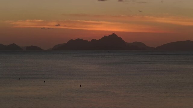 Aerial Left to Right Pan of Corong Corong Beach Sunset in El Nido, Philippines. Drone Lateral Tracking Shot of Limestone Karst Mountain Silhouettes and Orange Dusk Sky.