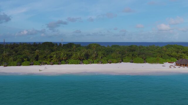 Aerial Maldives resort shows powder white sand and turquoise lagoon, palms, beach pavilions, umbrellas, a wooden jetty pavilion, two masts, gentle waves, guests strolling and launching small craft