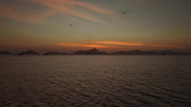 Aerial View Hovering Above Ocean Looking Toward Sunset at Corong Corong Beach in El Nido, Philippines. Cinematic Drone View of Golden Dusk Sky and Calm Sea Surface.
