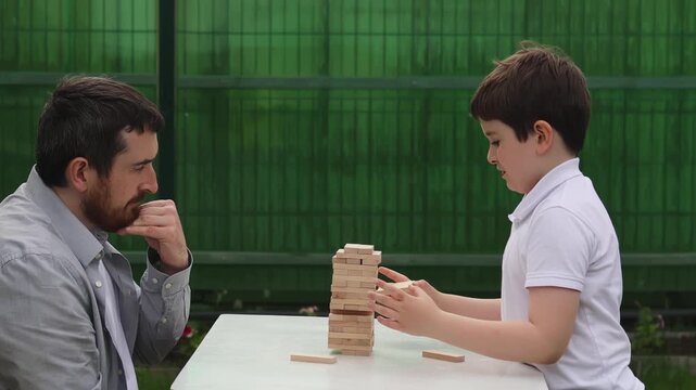 Wooden blocks. Green fence. Board game. Father and teenager. Slow motion video. High quality 4k footage