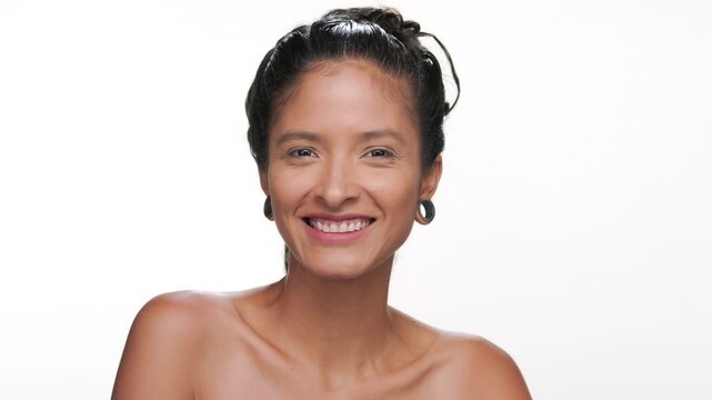 Close-up shot of positive latin woman with light brown smooth skin smiles for camera focusing on healthy skin on white background | Skin care advertisement