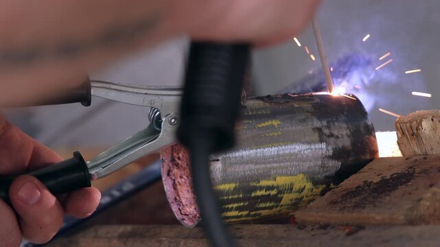 Close up of a welding ground clamp attached to a metal pipe on a workbench