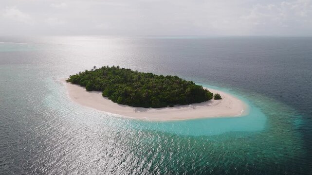 Aerial view of a Maldivian atoll and uninhabited island, fringing reef, crescent sand, palm scrub, turquoise lagoon, deep ocean, slow drone pan, soft daylight.