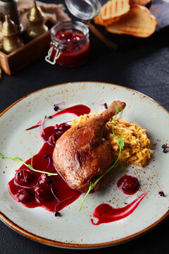 Baked duck leg with cherry sauce. Cherry sauce in small jar. An exquisite dish. Slices of white bread.