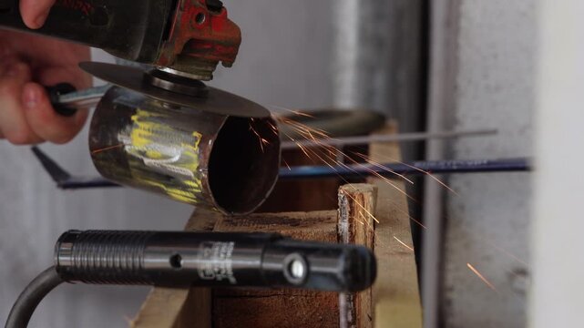 Close up of an angle grinder cutting a metal pipe with flying sparks in a workshop