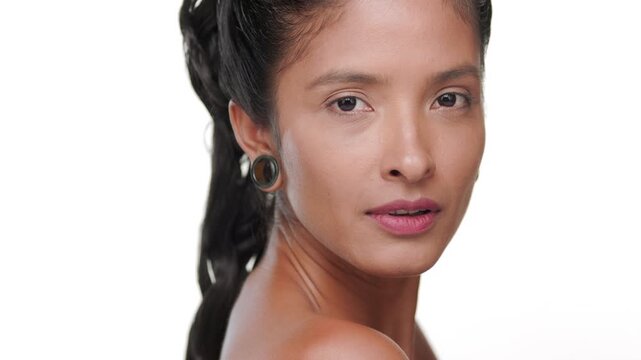 Big close-up shot of argentine woman with honey skin tone strokes her cheek showcasing revitalized skin against white background | Face care commercial